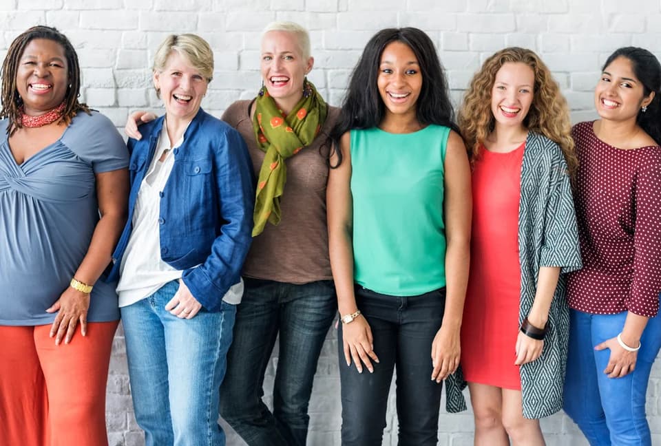 Six women standing together against a white brick wall
